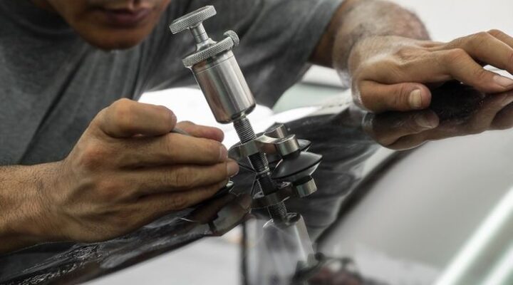 Mobile technician repairing a small rock chip on a car windshield at a homeowner's driveway in Allen, TX.